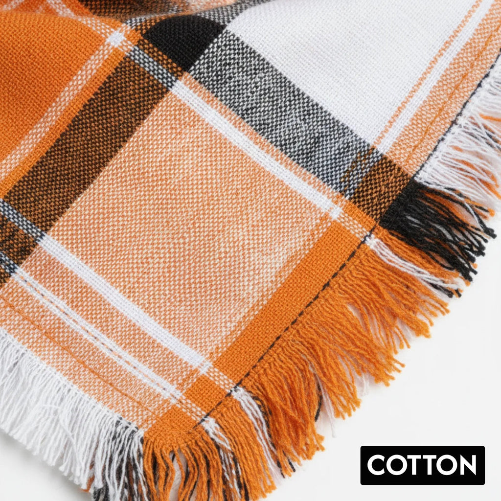 Orange, black, and white plaid cotton fabric with fringed edges, close-up view.