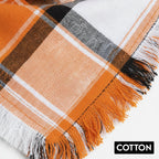 Orange, black, and white plaid cotton fabric with fringed edges, close-up view.