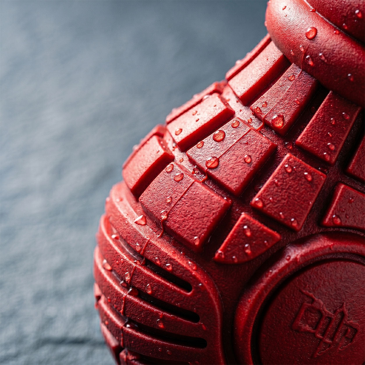 Close-up of Tailooo red rubber dog chew toy showing deep-grooved durable texture covered in water droplets, demonstrating waterproof and tough construction.