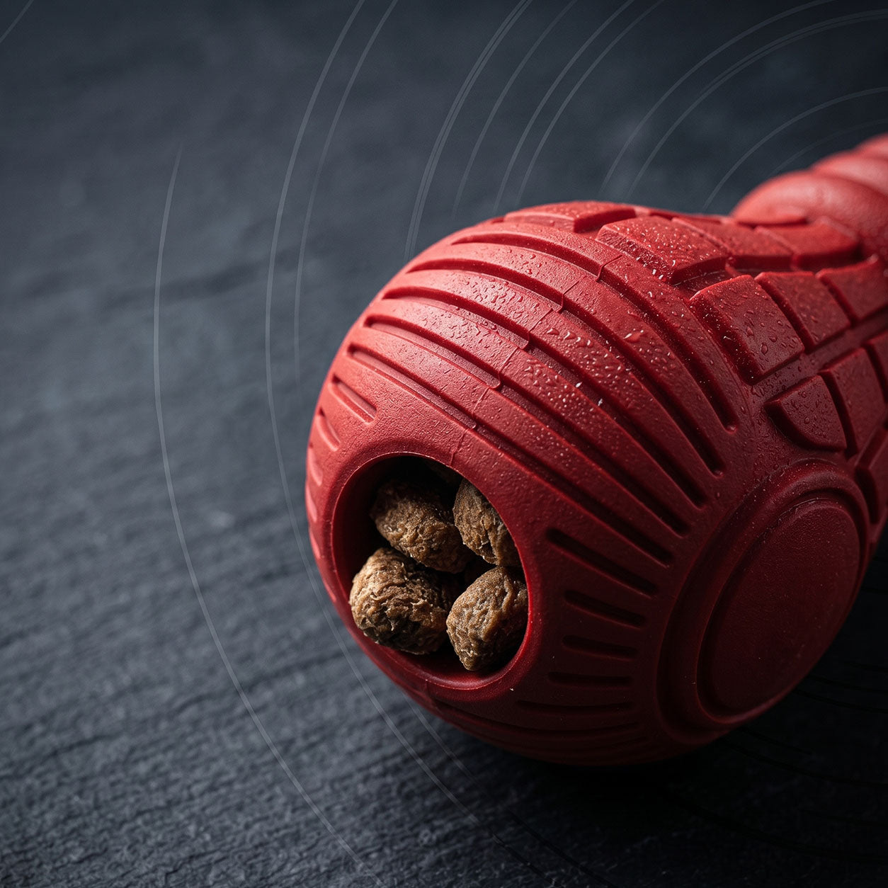 Tailooo red rubber dog chew toy on its side showing kibble treats visible through the hollow opening, with motion lines suggesting rolling movement.