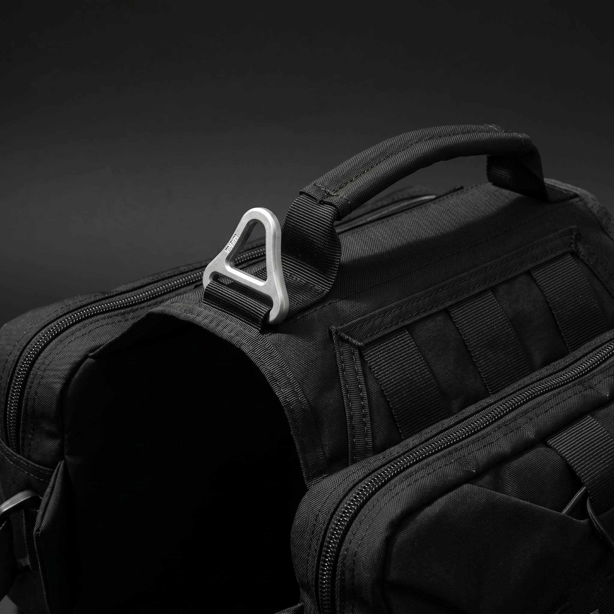 Close-up of Tailooo dog hiking pack top handle and aluminium alloy triangular D-ring on dark background, showing durable hardware and control handle design.