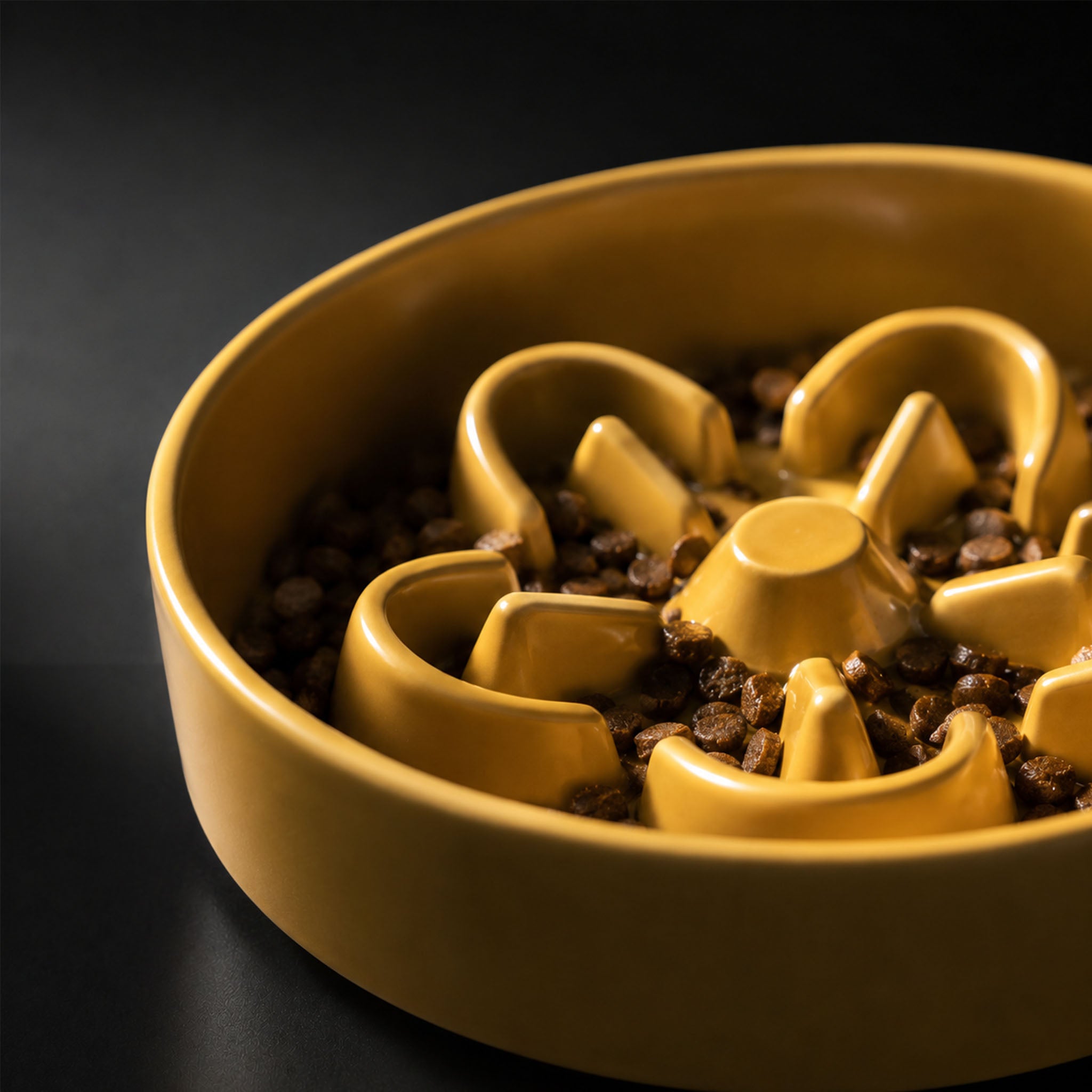 Top-down close-up of yellow ceramic slow feeder bowl filled with kibble, showing staggered maze ridges with 10–15mm height variation.